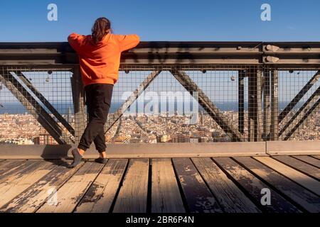 Vista posteriore di una ragazza adolescente che indossa una camicia con cappuccio arancione in piedi sul ponte. Posa rilassante. Contemplare il paesaggio urbano e pensare abou Foto Stock