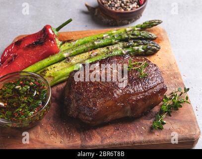 bistecca di manzo, montone arrosto con asparagi su un tagliere, salsa con olio d'oliva ed erbe, spezie, primo piano Foto Stock