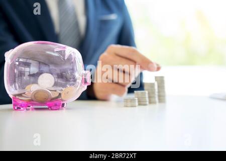 Close up di imprenditore moneta messa in piccoli salvadanaio , il concetto del risparmio e degli investimenti Foto Stock