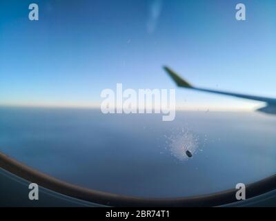 Colore immagine ravvicinata di un piccolo foro nella finestra di un aereo passeggeri, volare sopra le nuvole. Foto Stock