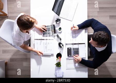 Alta Vista angolo di maschio e femmina imprenditori calcolo fattura con calcolatrice in ufficio Foto Stock