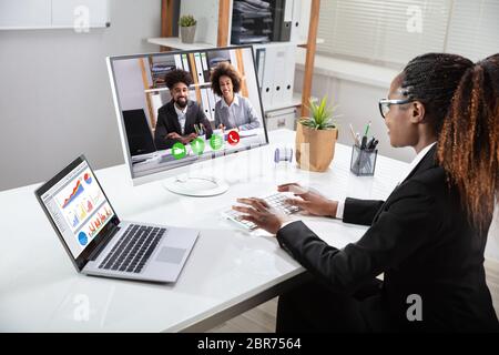 Sorridente giovane imprenditrice la videoconferenza con i suoi colleghi sul computer portatile vicino Foto Stock