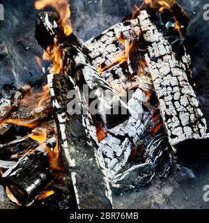 Carboni Ardenti e registri carbonizzati con piccole fiamme arancione in un barbecue fire in una vista ravvicinata pronti per la cottura del cibo Foto Stock