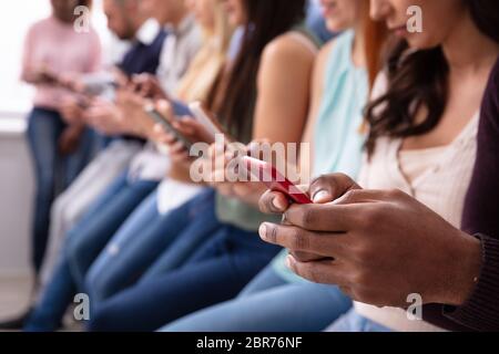 Multi-etnico Giovani appoggiata vicino a tavola in fila utilizza lo smartphone Foto Stock