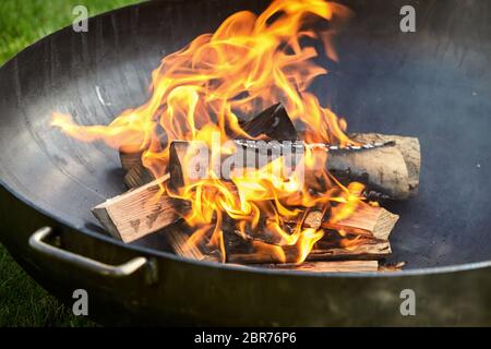 Registri annerita sul fuoco coperto di segni di bruciatura durante la seduta all'interno di metallo scuro barbecue durante cookout Foto Stock