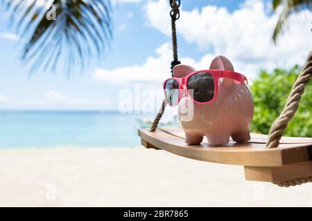 Close-up di Rosa Piggybank con gli occhiali da sole sul brandeggio in legno a Beach Foto Stock