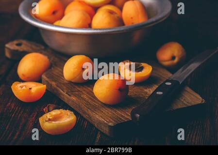 Mellow albicocche con il coltello su un vecchio tagliere di legno e metallo ciotola con frutti Foto Stock