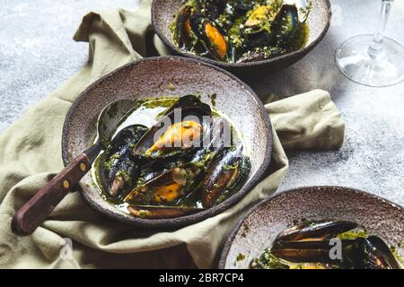 Cena in stile mediterraneo. Primo piano di tavola con cozze in salsa verde e vino bianco. Foto Stock