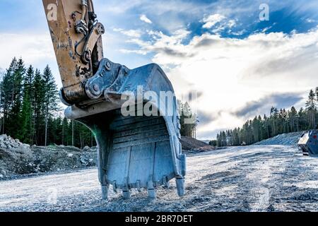 Primo piano vista posteriore presso la pala grande del bellissimo escavatore su una nuova strada non ancora pronta. Serata soleggiata con nuvole blu scuro, primavera, foresta mista con Foto Stock