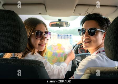 Vista posteriore di giovane coppia asiatica con donna utilizzando una mappa su un viaggio su strada per indicazioni e uomo che guida seduto in un'auto. Concetto di viaggio Foto Stock