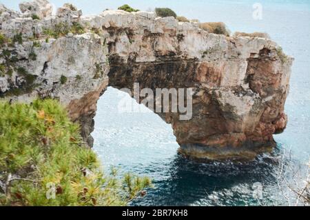 Es Pontas a Maiorca con barca ancorata nelle vicinanze del Mediterraneo. Maiorca Alba con yacht e arco di roccia vicino Santanyi. Maiorca Cala Llombar Foto Stock