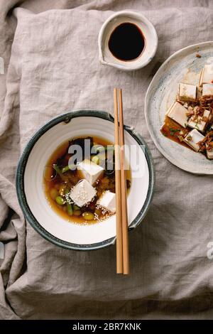 Zuppa giapponese di brodo miso con cubetti di tofu di seta, edamame di fagioli di soia, fagioli verdi in ciotola tradizionale con bastoncini di cotone su tovaglia di lino grigio. Din asiatico Foto Stock