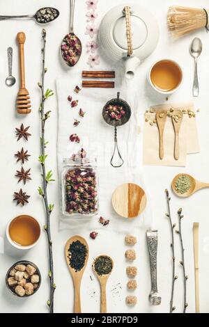 Disegno creativo con diversi tipi di tè in cucchiai di legno e argento, tisane e tazze, rami di primavera, miele, zucchero e spezie su tela d'epoca Foto Stock