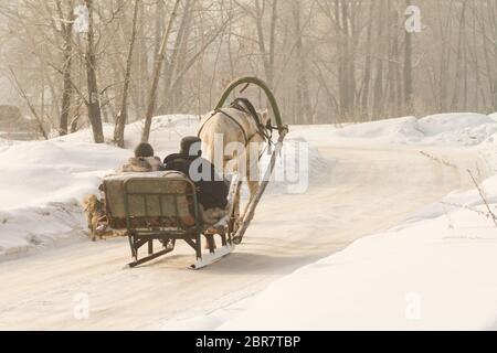 Un abitante di un villaggio in un villaggio va in una rudimentale slitta e corre a cavallo di una giornata invernale Foto Stock