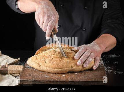 Chef in nero tagli uniformi cotta farina di frumento bianca pane ovale in legno marrone board Foto Stock