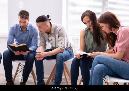 Gruppo di amici seduti insieme sulla sedia leggendo la Bibbia Foto Stock