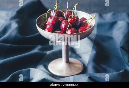 Le ciliege fresche in argento vintage vaso nel buio di sfondo di legno Foto Stock