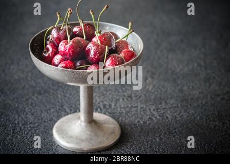 Le ciliege fresche in argento vintage vaso nel buio di sfondo di legno Foto Stock