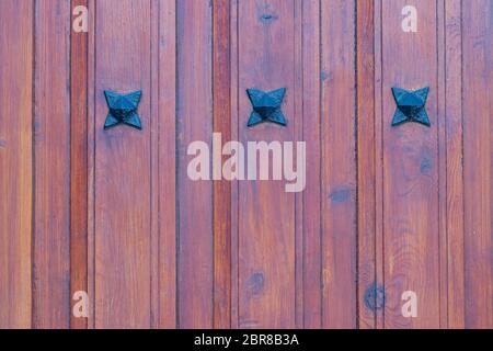 Texture di legno dello sfondo. Ingrandimento di un particolare di un legno marrone rosso porta di ingresso con tre stelle di metallo su tavole di legno. Macro. Foto Stock