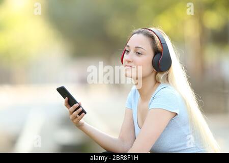 Ragazza rilassati ascoltando la musica con le cuffie e smart phone che guarda lontano seduto in un parco Foto Stock