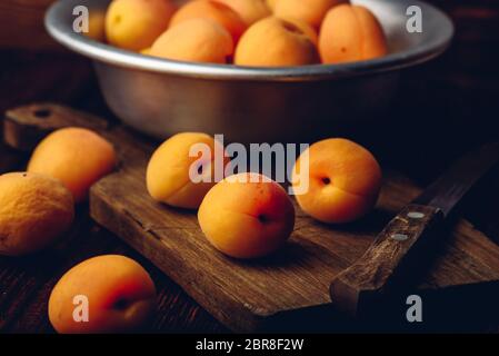 Mellow albicocche con il coltello su un vecchio tagliere di legno e metallo ciotola con frutti Foto Stock