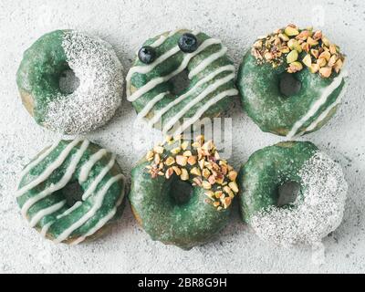 Vegan ciambelle con semi di Chia e rabboccato con sani spirulina smalto con pistacchio, noce di cocco essicata e mirtillo. Blu Verde spirulina ciambelle, su Foto Stock