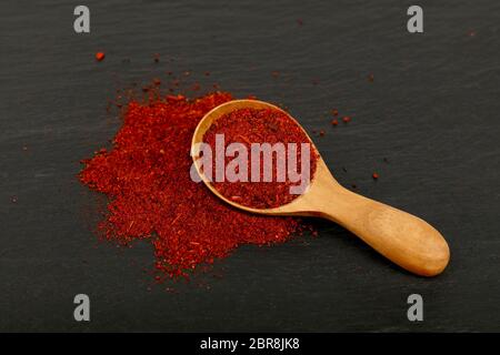 Close-up di legno un cucchiaio pieno di sole di massa essiccata di pomodoro o di peperoncino rosso su sfondo di ardesia nera scheda di cottura, ad alto angolo di visione Foto Stock