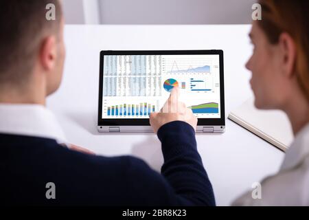Vista posteriore di imprenditore il lato rivolto allo schermo del laptop che mostra il grafico a barra su bianco scrivania Foto Stock