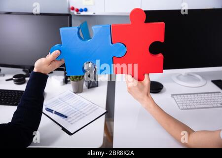 Close-up di due imprenditori la mano che regge il rosso e il blu Jigsaw Puzzle al posto di lavoro Foto Stock