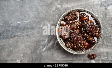 Deliziosa marmellata con coni di pino in una piccola ciotola. Dessert tradizionale siberiano - confettura di coni di pino giovani su sfondo grigio testurizzato. Vista dall'alto o appartamento la Foto Stock