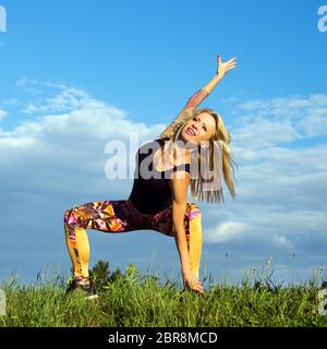 La bella donna bionda di mezza età sorridente si sta esercitando all'aperto sull'erba. Foto Stock