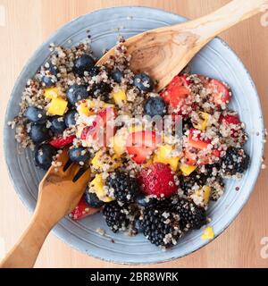 Blue ciotola riempita con insalata di frutta con la quinoa, fette di fragole, pesche noci tritate. more e mirtilli sulla superficie di legno, immagine 7 di 8 Foto Stock