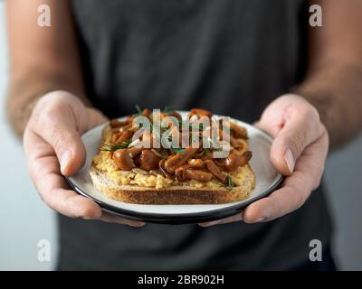 Mani tiene la piastra con vegan sandwich. Una sana appetiezer - pane integrale tostato con hummus di ceci e miele fungo funghi Foto Stock