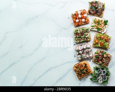 Assortimento di panini vegan su marmo bianco dello sfondo. Impostare diversi smorrebrod vegetariano. Vista superiore piatta o laici. Copia spazio per il testo. Foto Stock