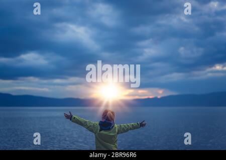 Trionfante bambina sollevando le mani in aria in alto mentre si sta in piedi sul grandi massi sulla riva del lago di Ohrid, Repubblica di Macedonia Foto Stock