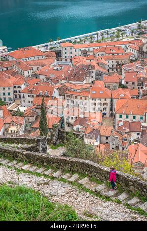 Bambina in rosa giacca impermeabile a piedi verso il basso sul sassoso sentiero e la scalinata che conduce alla fortezza di Cattaro sopra la città di Cattaro, Montenegro Foto Stock