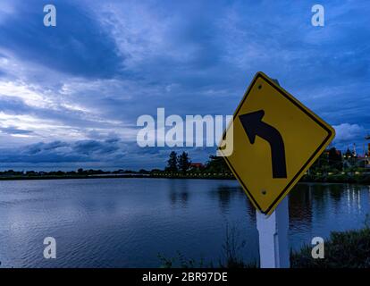 I segni sulla curva a sinistra puntano verso le nuvole. Il cielo dopo il tramonto Foto Stock