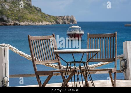 Sedie di legno dai vuoti di un ristorante esterno tavola su una piattaforma di coperta in Agios Nikolaos beach sull'isola di Zante, Grecia Foto Stock
