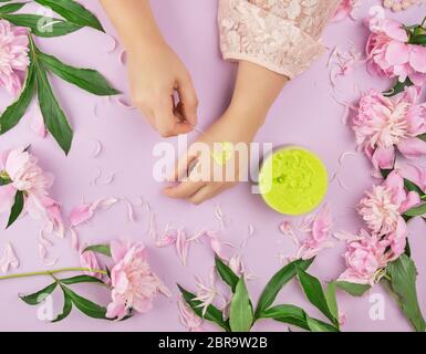 Due mani femminili e un vaso con fitta macchia verde e rosa peonie fiorite con foglie verdi, concetto di anti-invecchiamento delle procedure per il ringiovanimento e Foto Stock