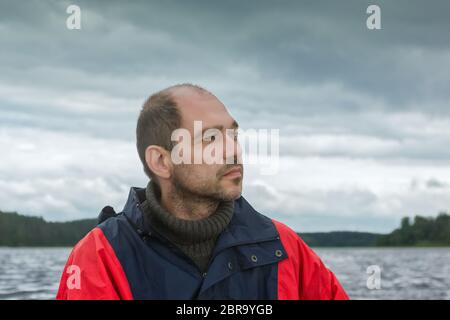 Ritratto di un uomo maturo pensivo bearded contro il cielo nuvoloso e il lago tempestoso. Messa a fuoco selettiva su primo piano, sfondo naturale sfocato Foto Stock