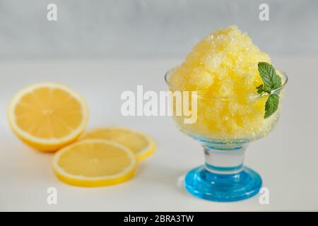 Dessert giapponese kakigori limone in una ciotola di vetro e fette di limone sullo sfondo Foto Stock