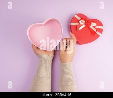 Ragazza apre una confezione regalo rossa su uno sfondo viola, vista dall'alto, il concetto di regali Foto Stock