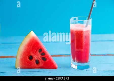 Un pezzo di cocomero e smoothie,spremuta di anguria succo in un vetro trasparente su un blu sullo sfondo di legno Foto Stock