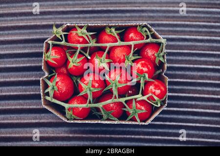 Scatola di pomodori freschi maturi cocktail di ciliegia rossa tipo per la vendita in un mercato. Immagine in stile retrò vintage. Imballaggio della carta ecologico. Foto Stock