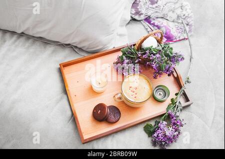 Vassoio in legno di caffè e candele con fiori sul letto. lenzuola