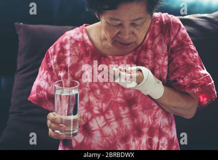 Senior donna asiatica prendere la pillola medicina a portata di mano mentre è seduto sul divano di casa Foto Stock