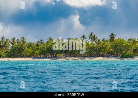 Spiaggia tropicale sovraesposta con sabbia bianca, palme, oceano turchese contro cielo nuvoloso con onde nella soleggiata giornata estiva. Sfondo perfetto Foto Stock