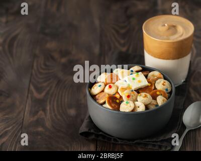 Mini pancake cereali e caffè dalgona su sfondo di legno marrone, spazio copia. Cibo e bevande alla moda - minuscoli pancake serviti spruzzano e montato caffè istantaneo con latte o caffè coreano dalgona Foto Stock