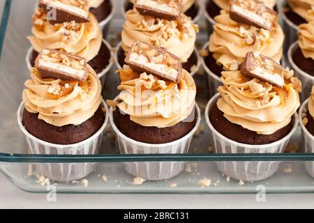 Cupcake con crema di formaggio al burro di arachidi, morsi di cioccolato, caramello salato e noci tritate. Sfondo semplice Foto Stock