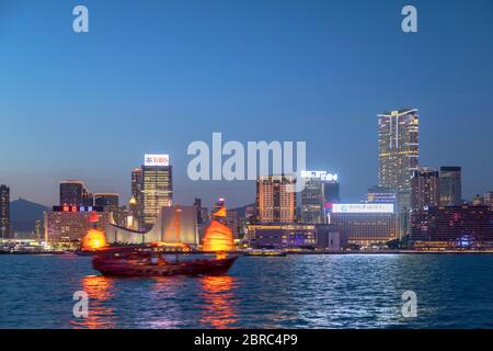 Skyline di Tsim Sha Tsui e barca spazzatura al tramonto, Hong Kong Foto Stock